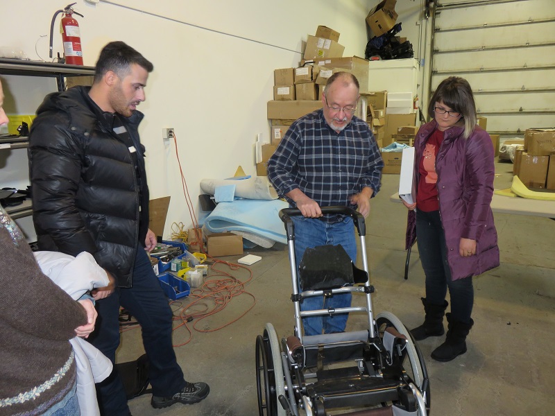 Wayne Hanson demonstrates how to adjust the wheelchair as Ilir (L) and Fjolla (R) observe